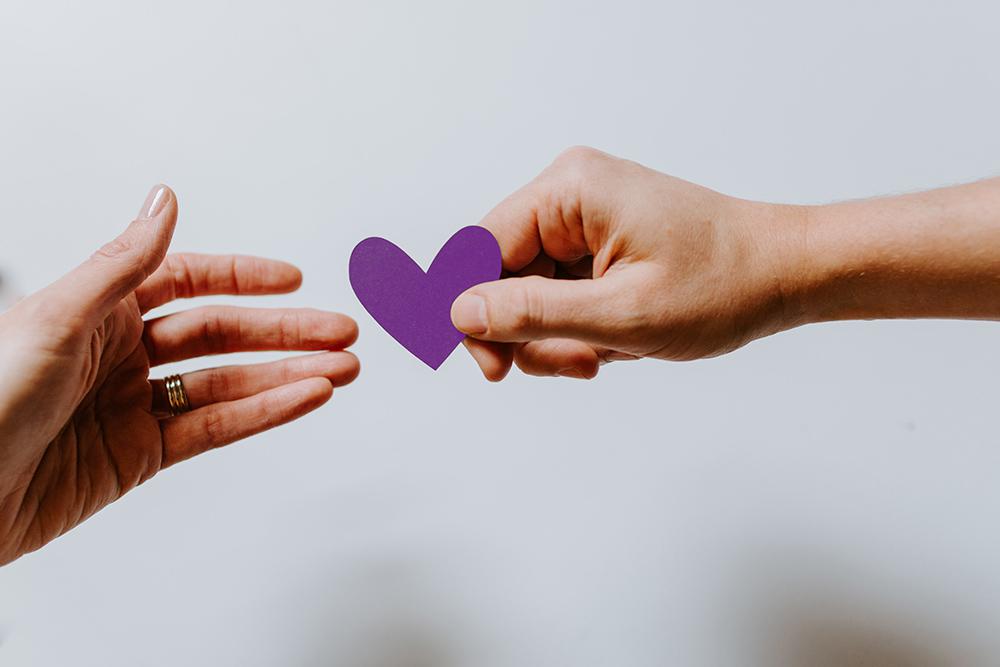 One hand passing a purple paper heart to another hand
